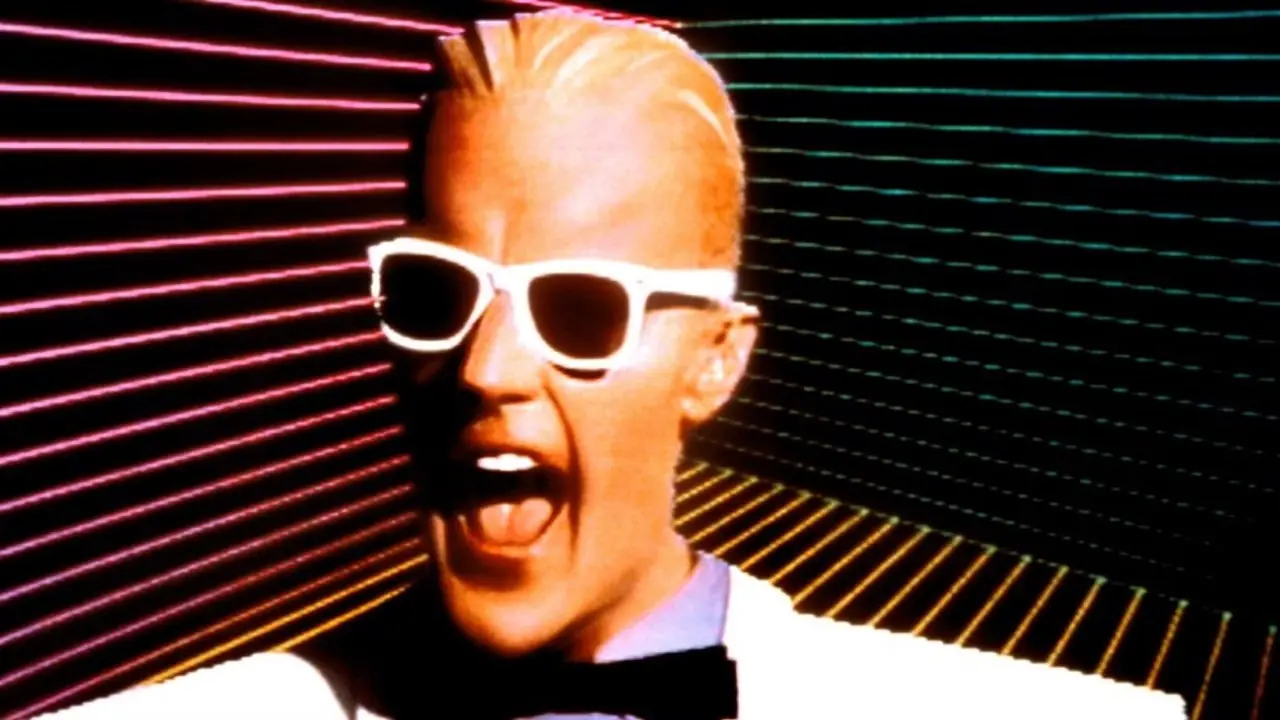 Max Headroom يبتسم أمام خلفية على طراز الثمانينيات.