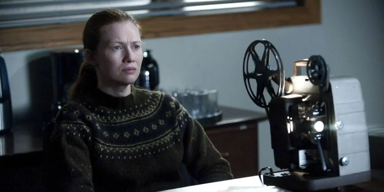 Mireille Enos como Sarah Linden sentada en una silla y mirando una proyección de The Killing. Mireille Enos como Sarah Linden sentada en una silla y mirando una proyección de The Killing.
