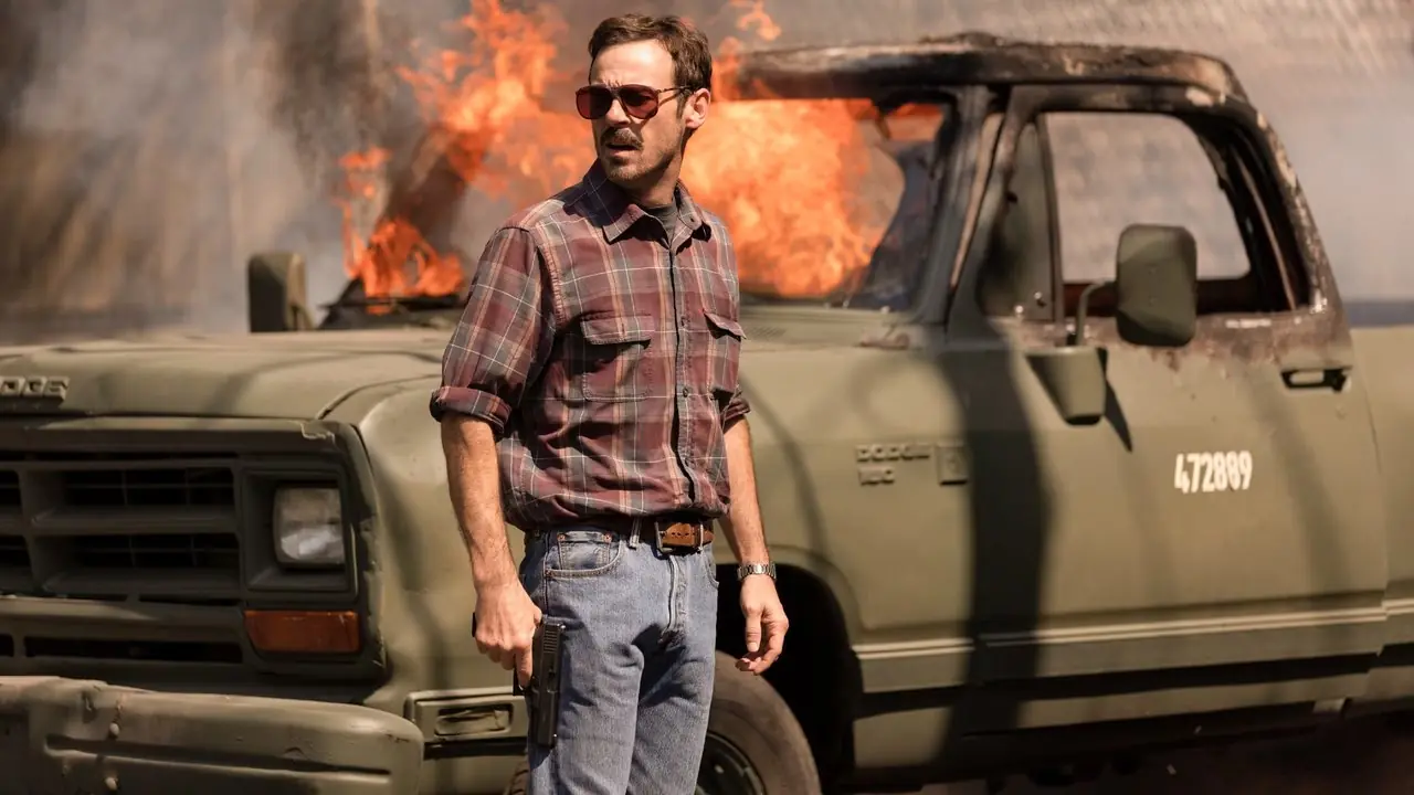 Scoot McNairy como Walt Breslin na frente de um carro em chamas em Narcos México