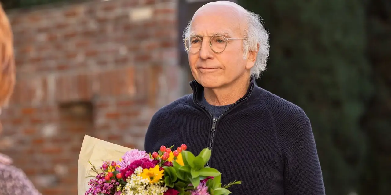 Larry David kijkt geïrriteerd terwijl hij bloemen vasthoudt in Curb Your Enthusiasm seizoen 11