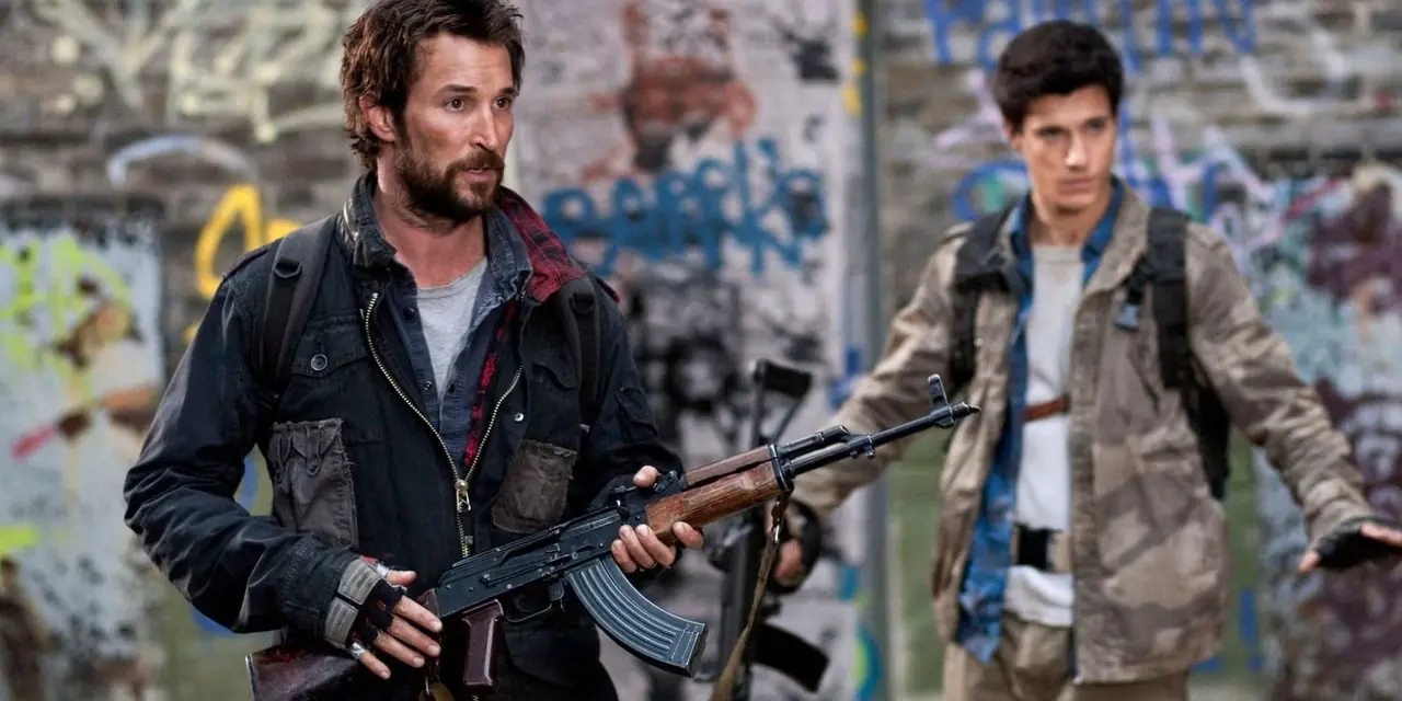 Tom Mason (Noah Wyle) sosteniendo un rifle de asalto con Hal Mason (Drew Roy) sosteniendo sus manos en alto en el fondo, en Falling Skies. Tom Mason (Noah Wyle) sosteniendo un rifle de asalto con Hal Mason (Drew Roy) sosteniendo sus manos en alto en el fondo, en Falling Skies.