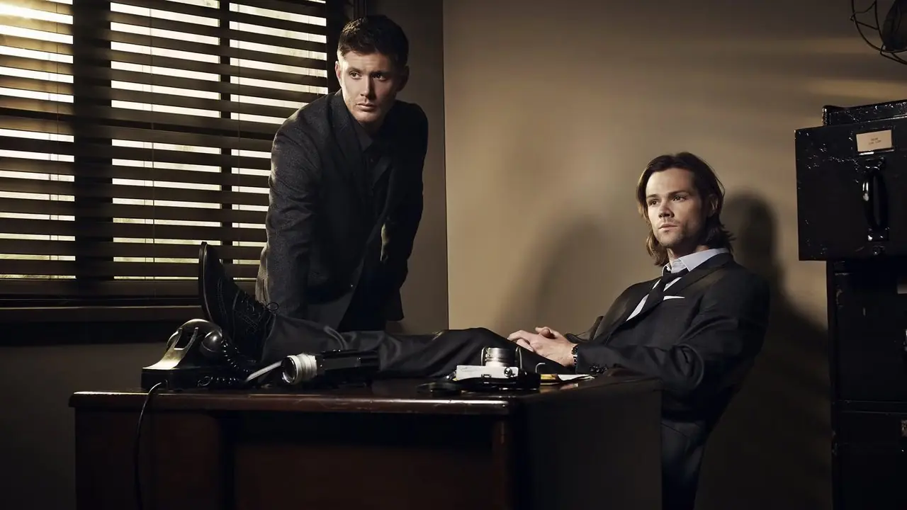 Übernatürliche Werbeaufnahme mit Sam und Dean in Anzügen an einem Schreibtisch. Übernatürliche Werbeaufnahme mit Sam und Dean in Anzügen an einem Schreibtisch.