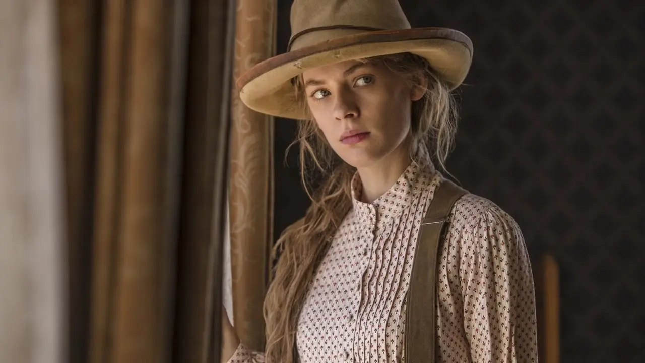 Tess Frazer parada junto a una ventana con un sombrero de vaquero en Godless