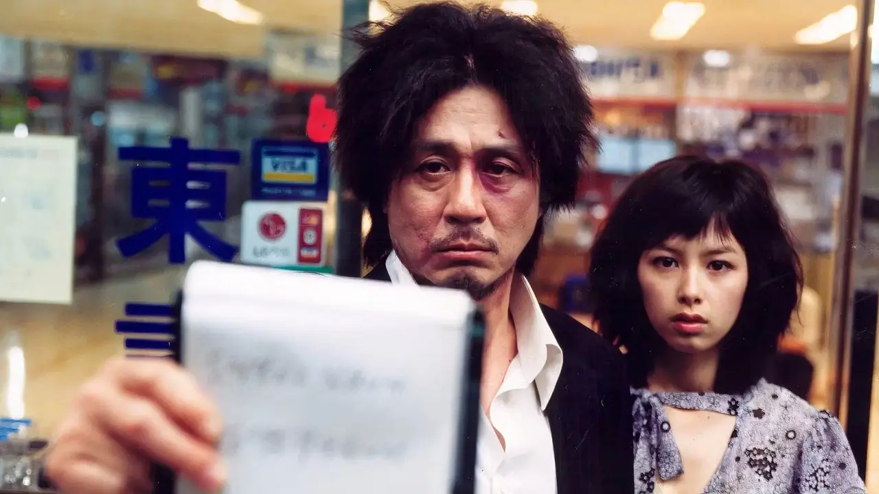 Dae-su hält ein Notizbuch in der Hand, während Mi-do in Oldboy (2003) hinter ihm steht.