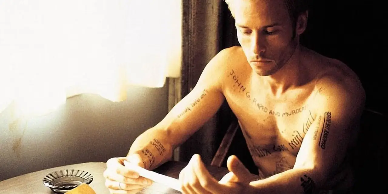 Guy Pearce als Leonard Shelby zit aan een tafel in Memento.
