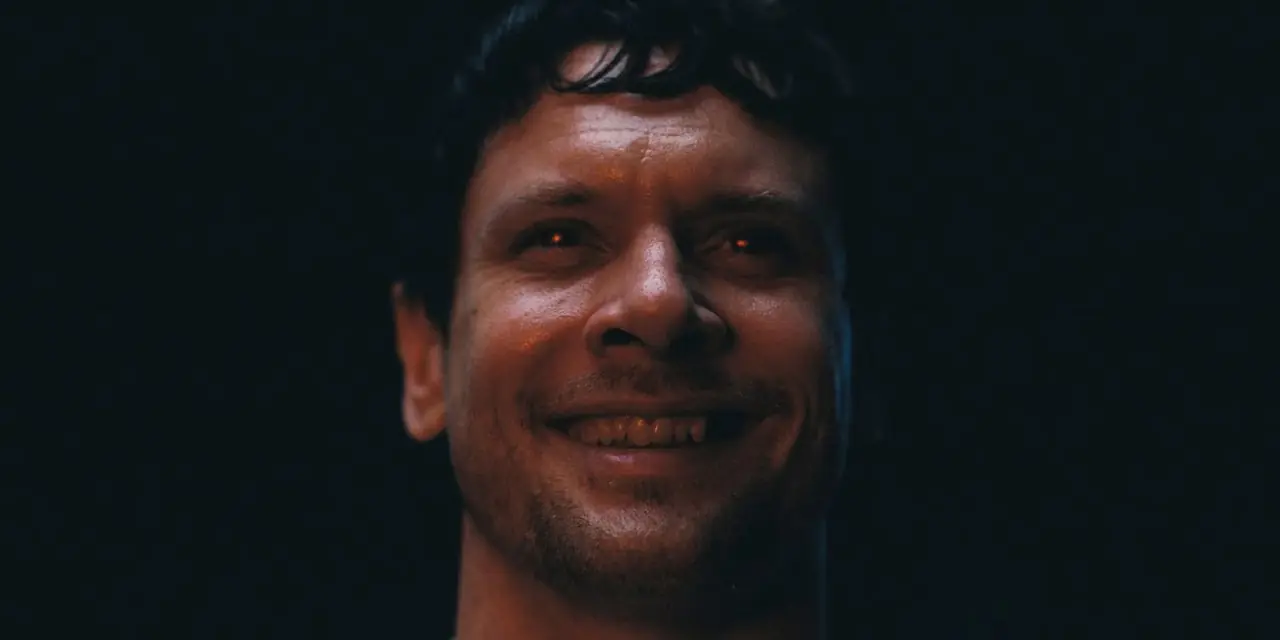 Jack O'Connell lächelt mit leuchtend roten Augen in Sinners