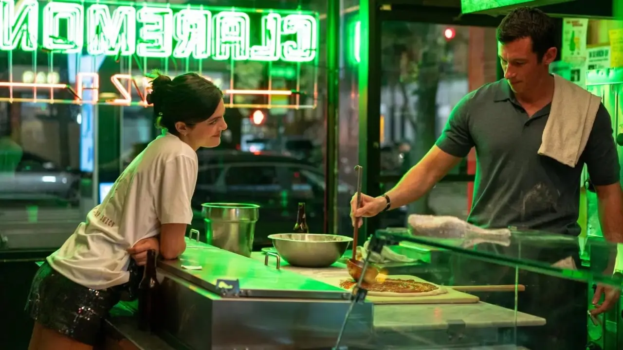 Monica Barbaro se penche sur le comptoir pendant que Callum Turner prépare une pizza dans One Night Only Movie
