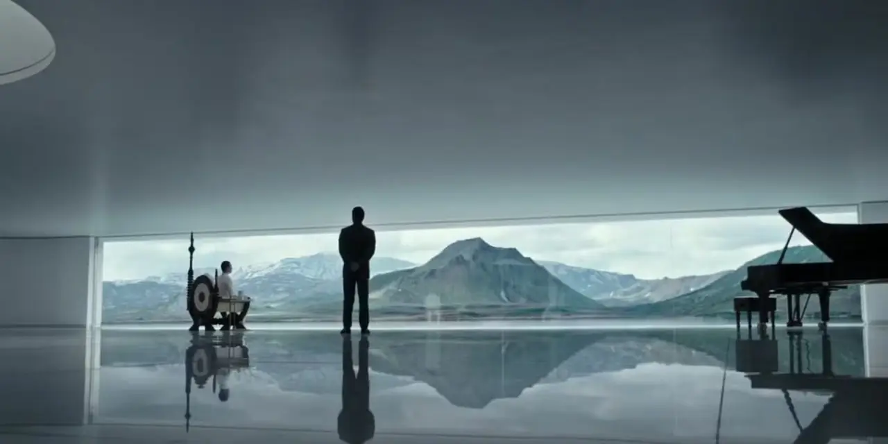 Alien: Covenant의 도입부 시퀀스 스틸입니다. 거울이 깔려 있고 흠집 하나 없는 바닥이 있는 넓은 방에서 Weyland는 블라인드 아래 산의 경치를 내려다보는 휠체어를 타고 있습니다. 데이비드는 등 뒤에 손을 얹고 그의 옆에 서 있습니다.