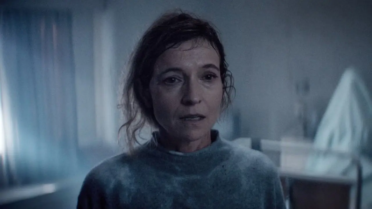 Une femme qui a l'air effrayée pendant que quelqu'un dans un drap sur un lit d'hôpital s'assoit dans Evil Dead Burn
