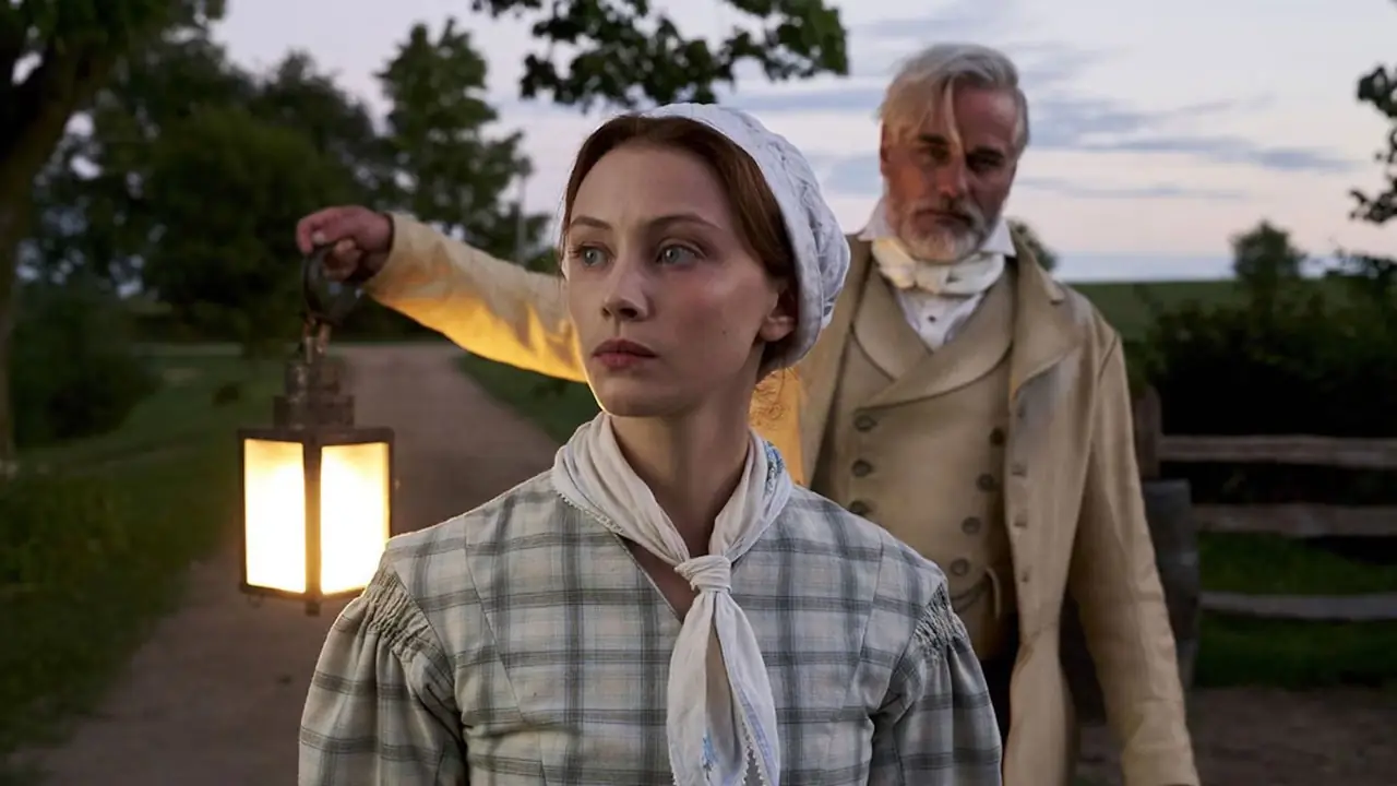 Un homme tenant une lanterne et une femme en tenue coloniale d'époque dans Alias Grace de Netflix. Un homme tenant une lanterne et une femme en tenue coloniale d'époque dans Alias Grace de Netflix.