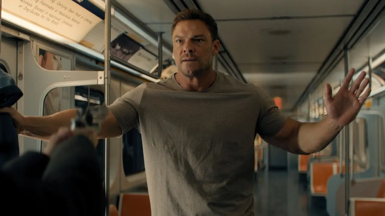 Alan Ritchson como Jack Reacher, luciendo asustado en el metro, con las manos en alto. Alan Ritchson como Jack Reacher, luciendo asustado en el metro, con las manos en alto.