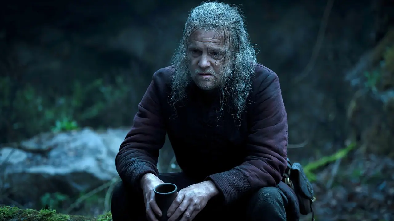 Tom Bennett's Ulf ziet er somber uit terwijl hij met een kopje in zijn handen zit in seizoen 3 van House of the Dragon