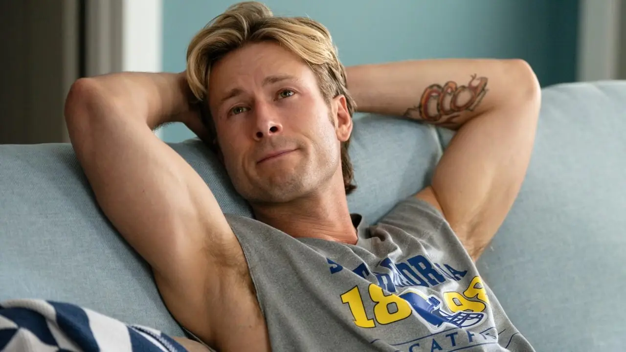Glen Powell exhibe ses muscles avec ses bras derrière la tête dans Chad Powers