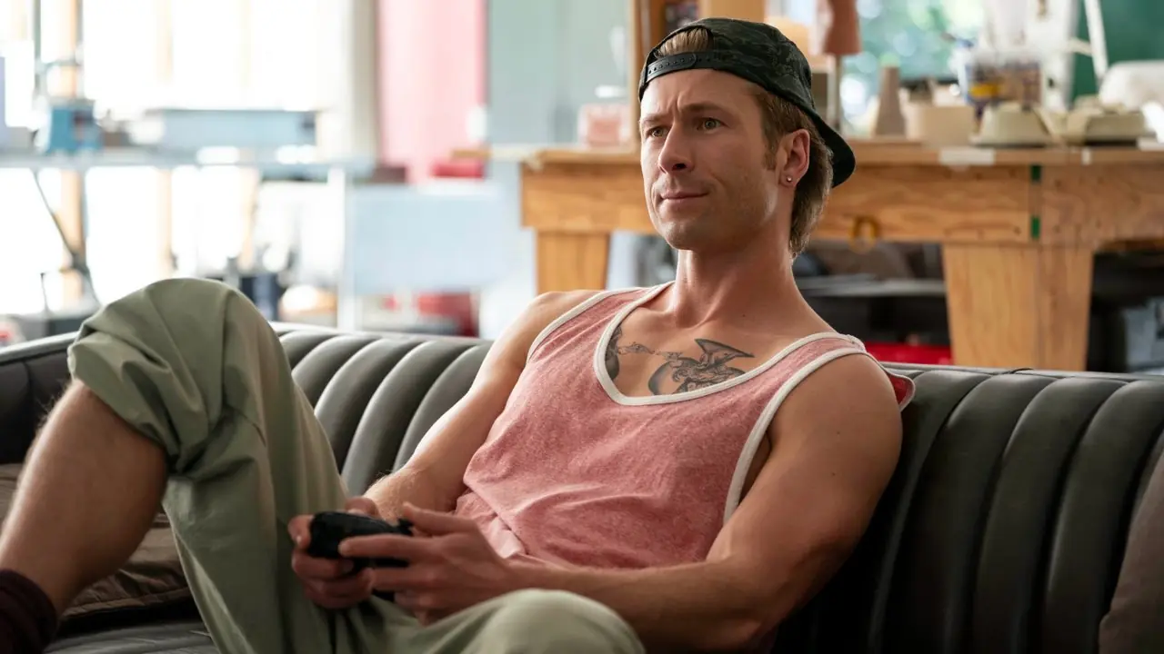 Chad Powers (Glen Powell) sur un canapé tenant une manette de jeu vidéo dans Chad Powers