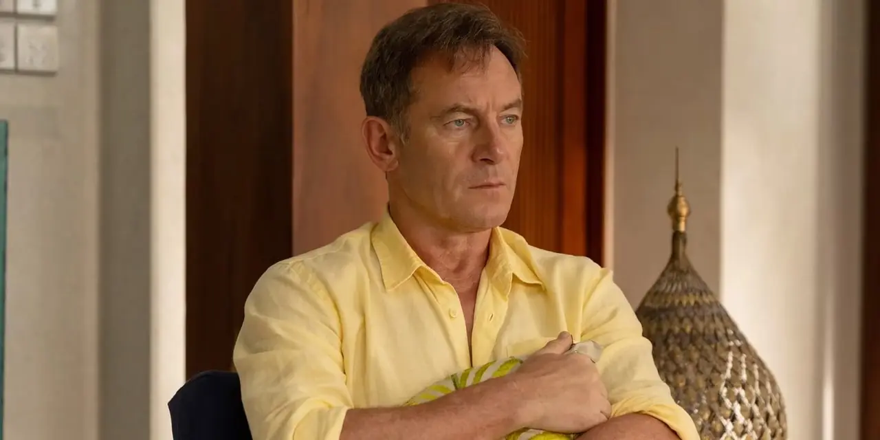 Jason Isaacs, The White Lotus'un 3. sezonunda elinde yastık tutan ve sandalyede oturan dikkati dağılmış görünen Timothy rolünde